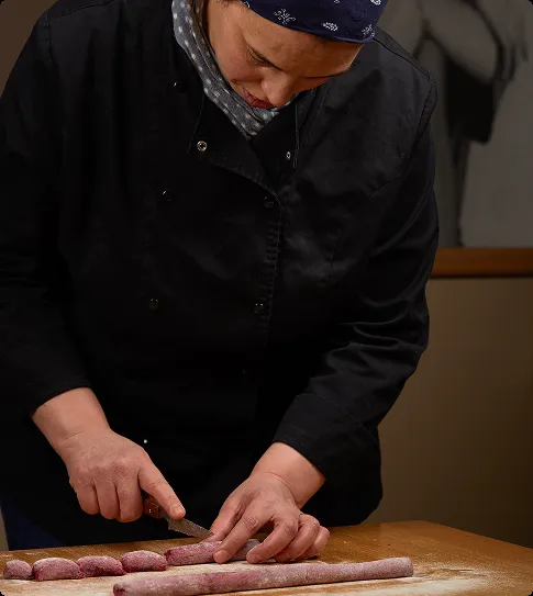 Une cuisinière découpe une pâte colorée à la main.